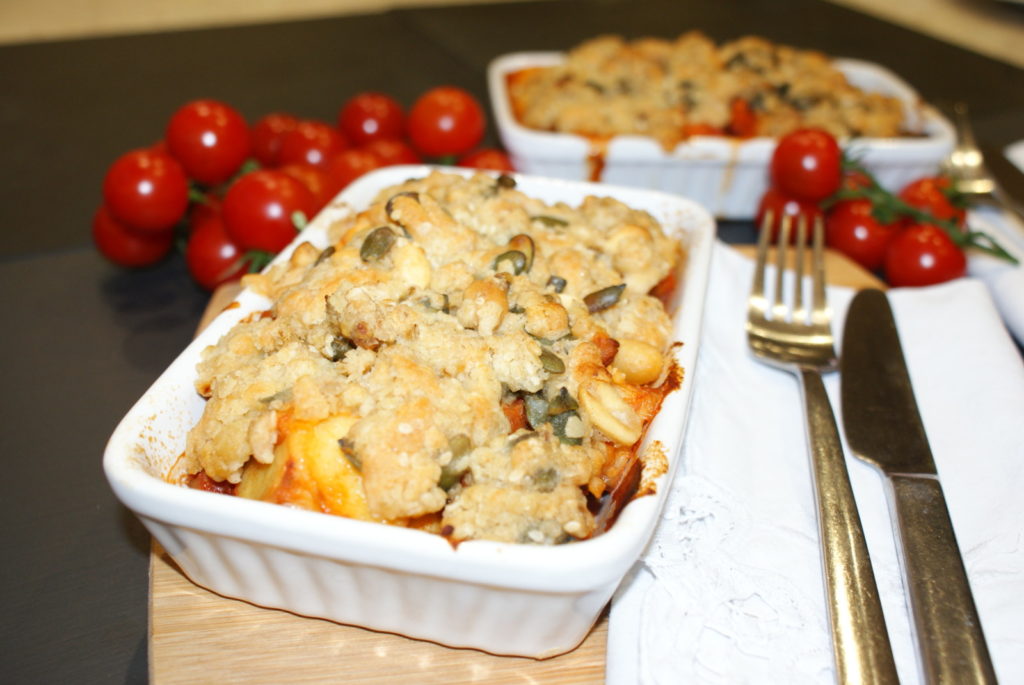 vegetable crumble in a white dish, with tomatoes in the background