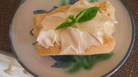 garlicky soft cheese on a pice of baguette on a white and blue plate.