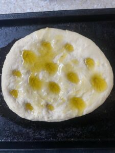An unbaked focaccia bread, with dimples filled with olive oil.