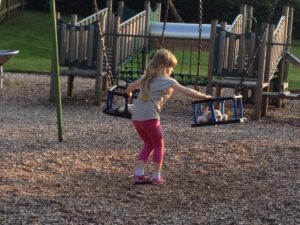 a young girl in a playground, wearing pink leggings and a stripy t-shirt.