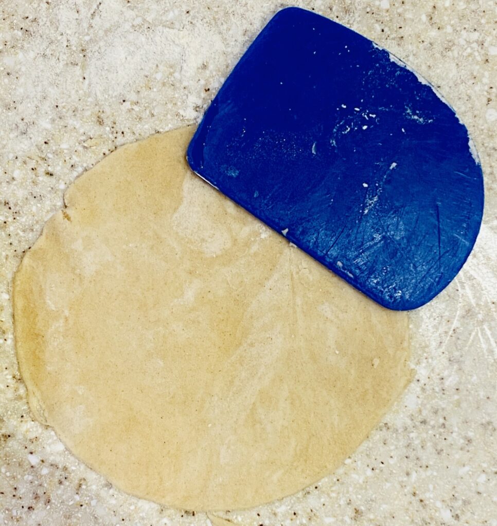 a small circle of raw pastry with a blue plastic trimmer