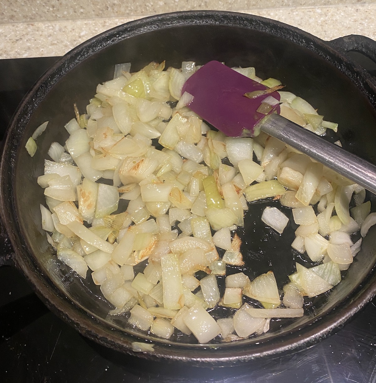 Onions frying in a cast iron pan, with a purple silicone spatula in the top right. 