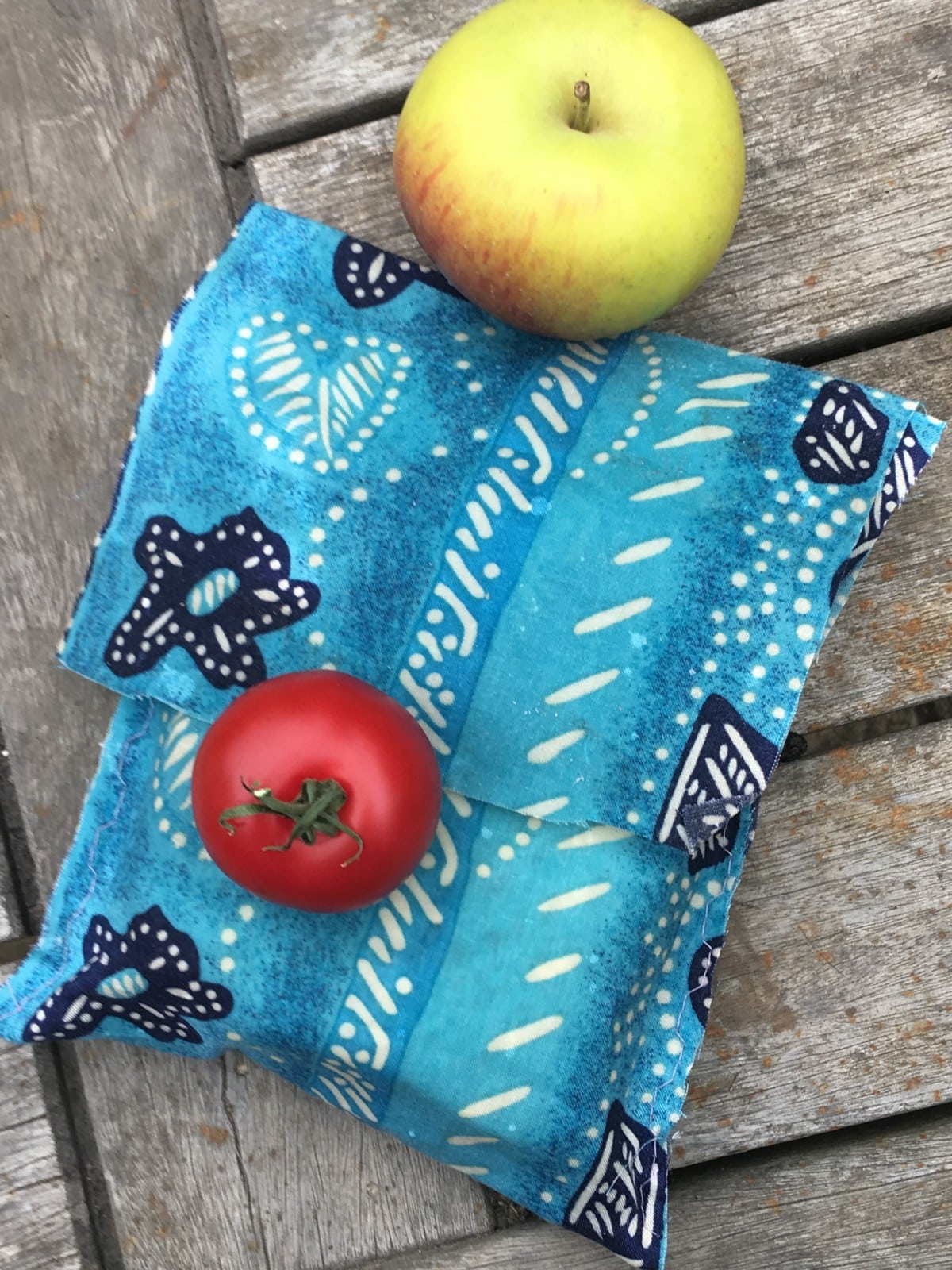 a beeswax sandwich bag, containing a sandwich. An apple and tomato are nearby.