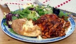 Honey and Soy chicken on a blue patterned plate with baked potato and sala