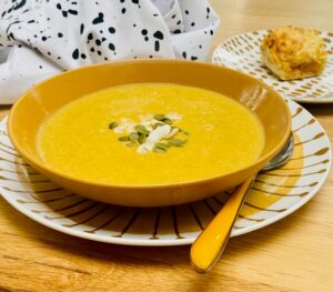 spicy red lentil soup in a mustard coloured bowl with a spoon, both resting on a mustard striped plate.