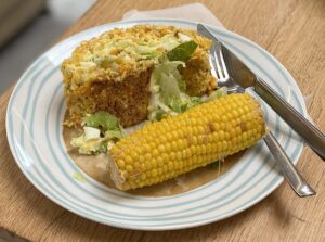 a slice of vegetable roulade on plate with a corn cob.