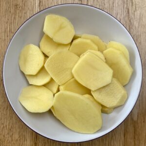 a white dish containing uncooked potato slices.