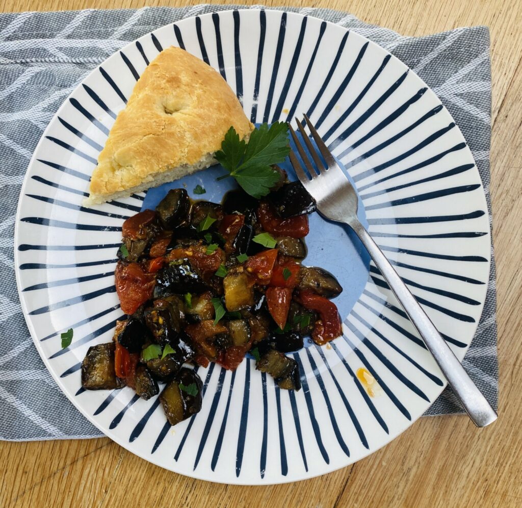 aubergine ragu on a blue patterned plate with a piece of focaccia.