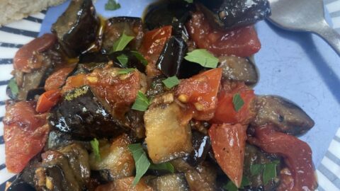 aubergine & tomato ragu on a blue patterned plate, with a piece of focaccia on the side.