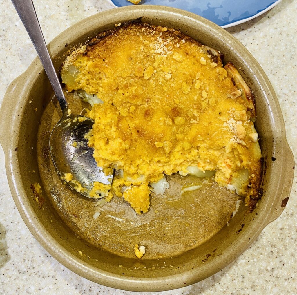 swede mash on a bed of potato slices in a pottery dish, with a spoon. 