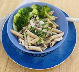The base of the crumble stored through wholemeal penne. With broccoli on the side. In a blue bowl, on a blue plate, with a white fork tucked into one side.