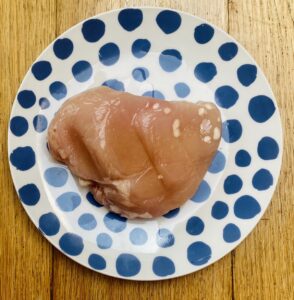 a fresh chicken breast on a blue spotted tea plate.