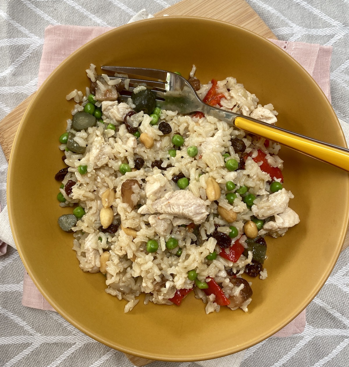 brown rice and chicken salad in a mustard coloured flat profile bowl, with a mustard coloured handle fork in one side.