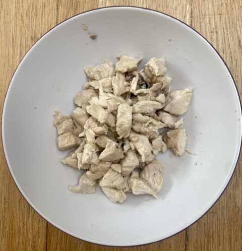cooked chicken, cut into small pieces, in a white bowl.