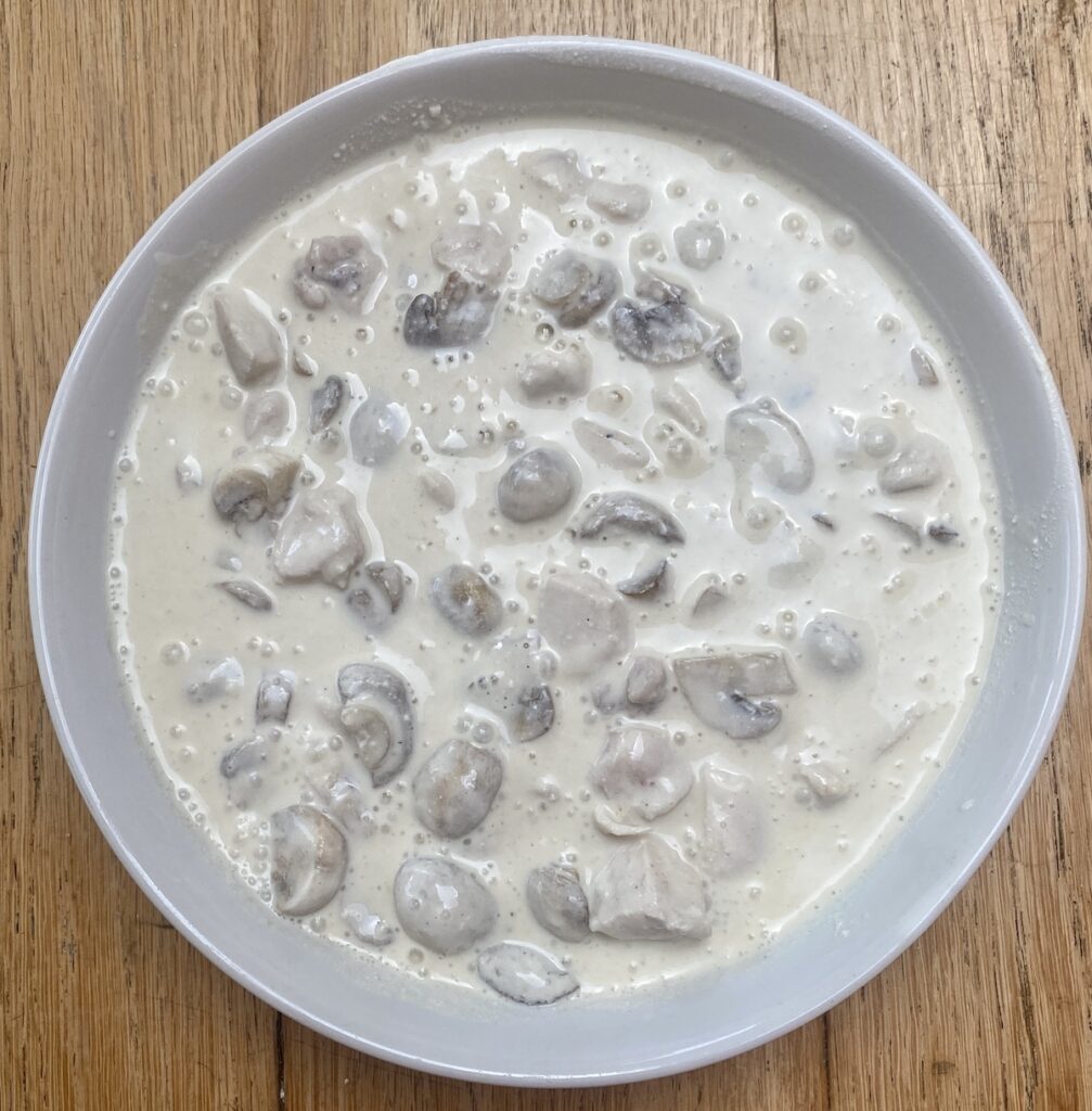cooked mushrooms, soft cheese and water in a white dish.