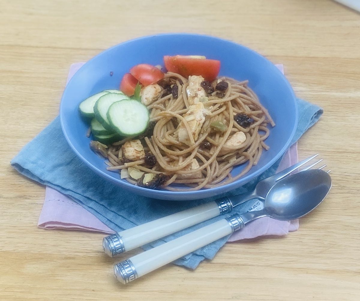Healthy chicken spaghetti in a blue bowl with white handled cutlery, on a blue napkin and a pink napkin.