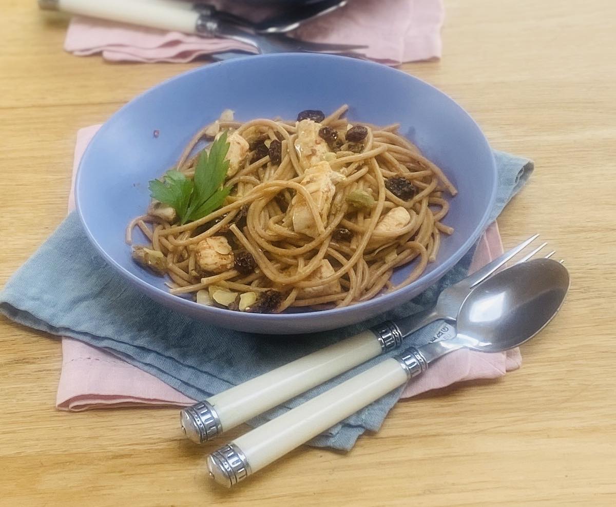 Sicilian pasta in a blue bowl, with white handled cutlery, on a blue napkin and a pink napkin.