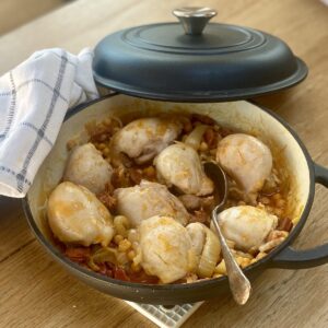 chicken and chorizo casserole in a black cast iron dish. The lid is propped on top, with a grey checked tea towel folded underneath.