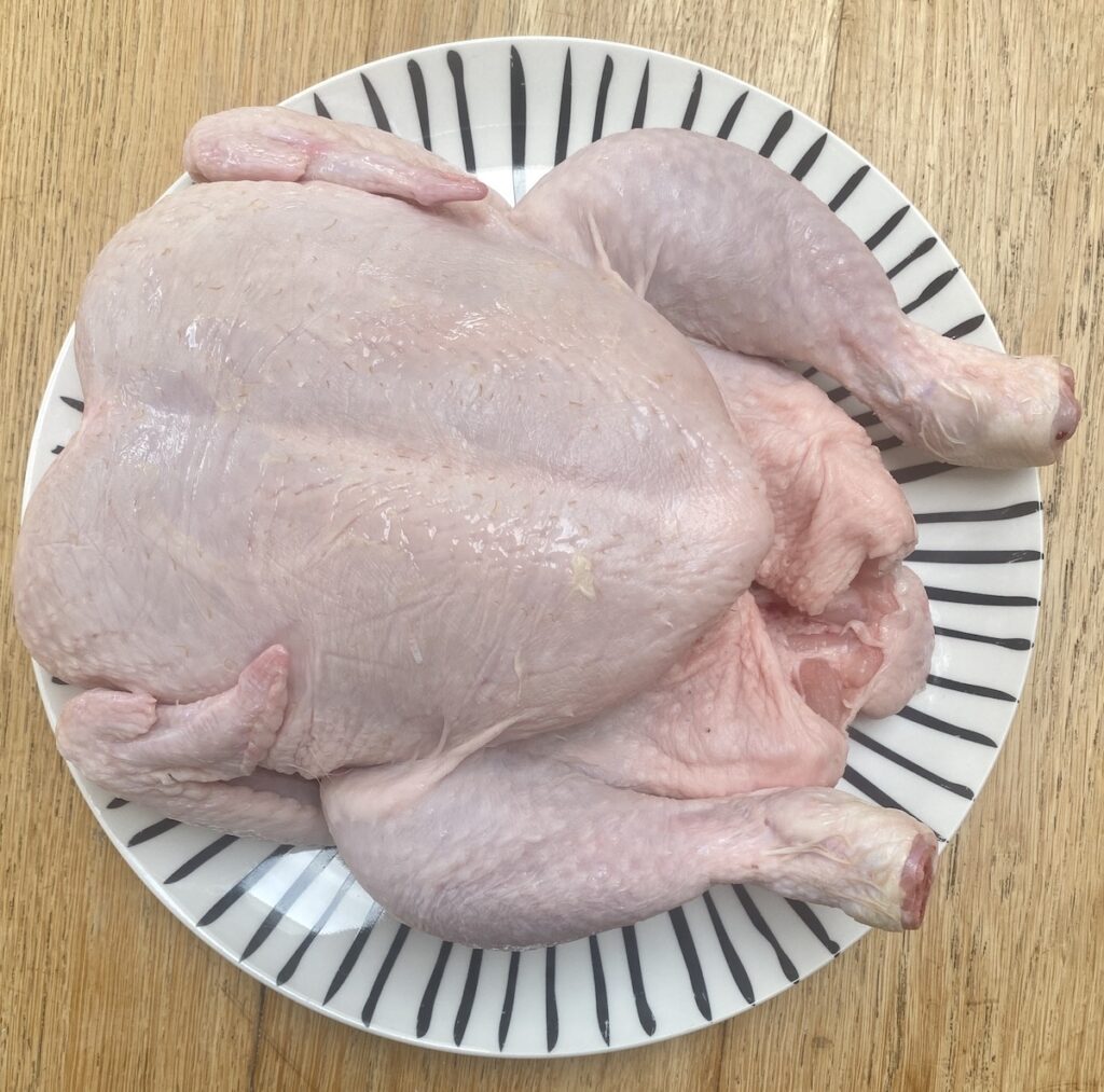 a whole, raw, chicken on a plate with a pattern of stripes on it.