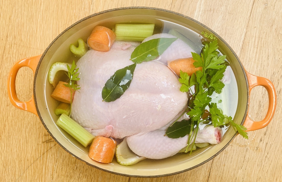 a whole chicken and some vegetables covered with water in a large pot.