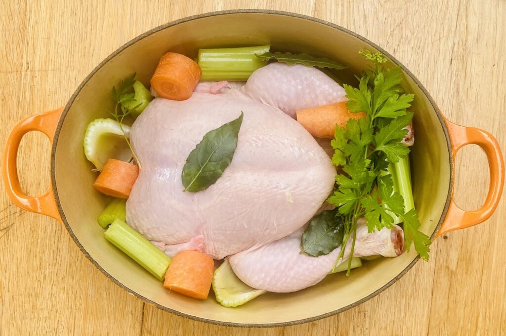 a whole chicken and some vegetables in a large pot. 