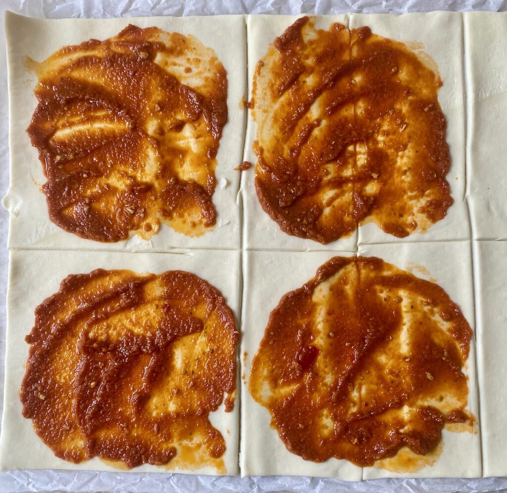 Puff pastry squares with red pesto spread over.