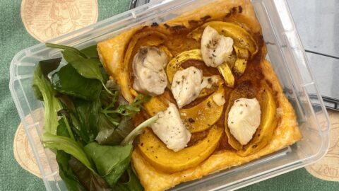 roast pumpkin tart in clear plastic lunchbox, resting on the lid. All on a green tea towel