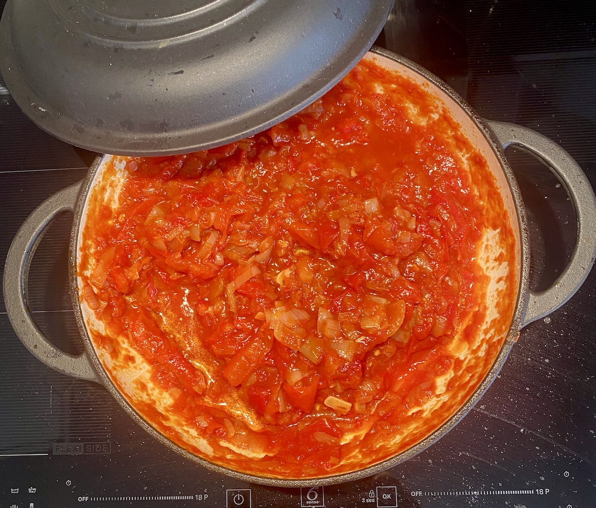 peperonata in a black saucepan, with lid on one side. 