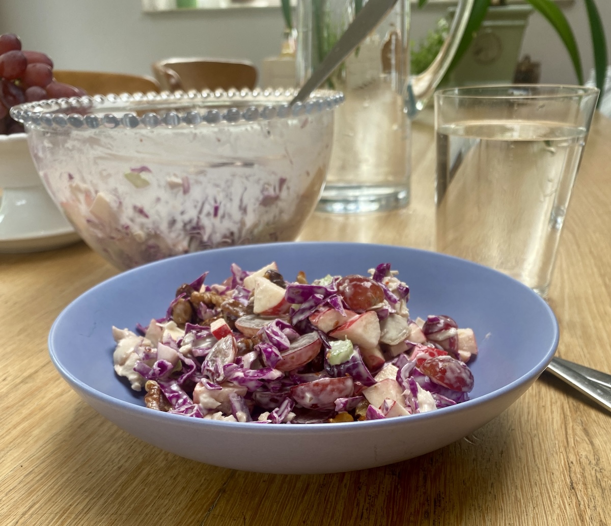 a vegan Waldorf salad in a blue bowl with a glass bowl nearby. 