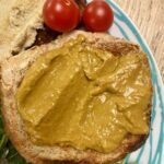 tomato curd on wholemeal toast, on a blue striped plate, with dressed leaves and 2 cherry tomatoes.