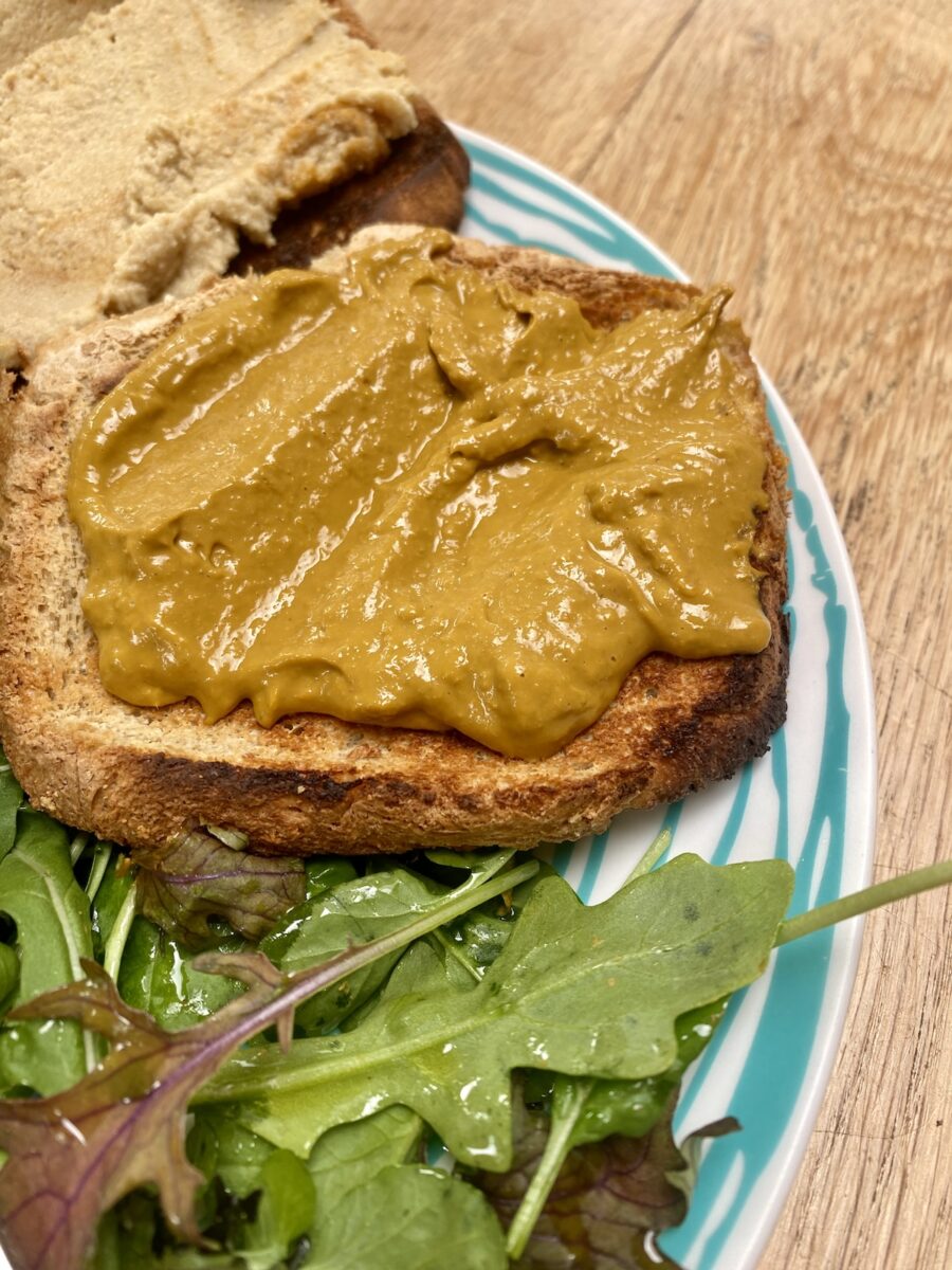 tomato curd on wholemeal toast, on a blue striped plate, with dressed leaves.