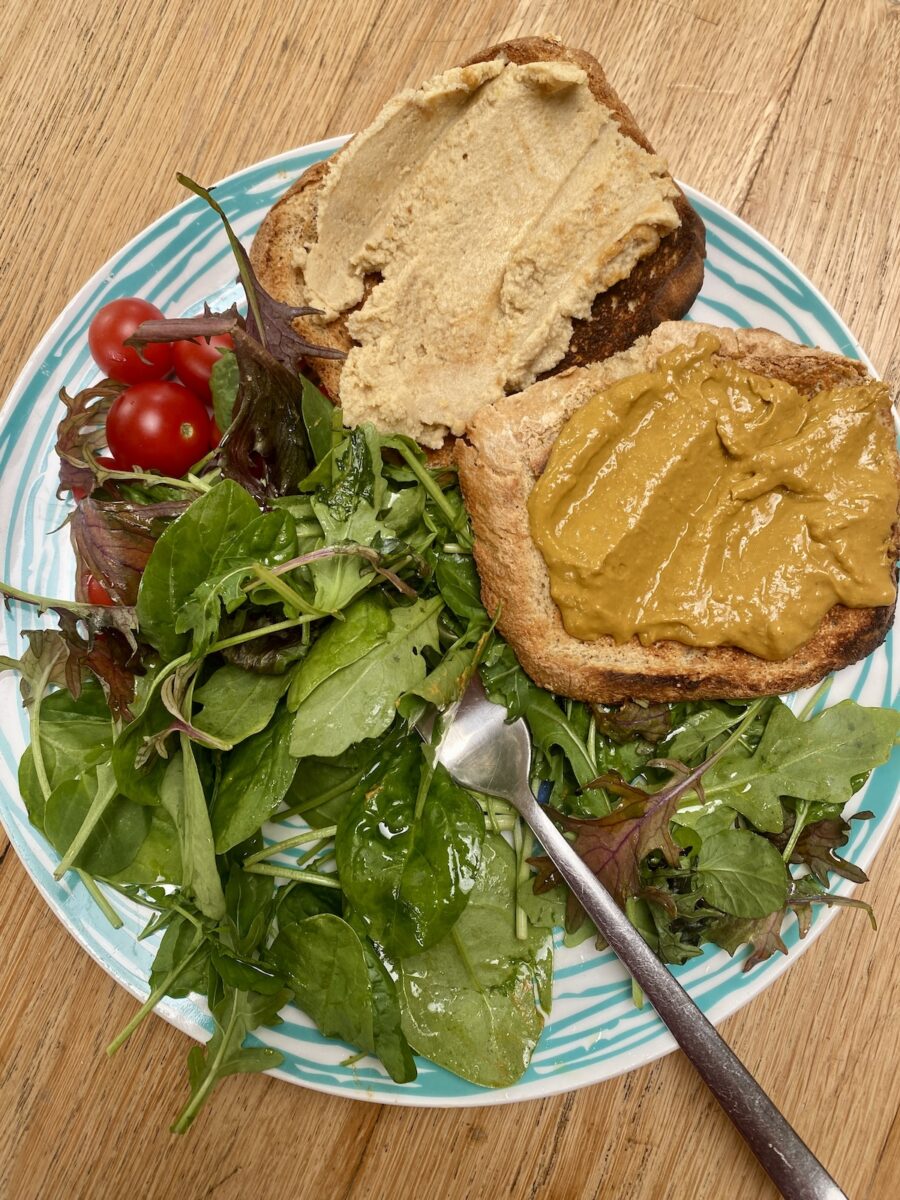 tomato curd on wholemeal toast, with hummus on toast, on a blue striped plate, with dressed leaves and cherry tomatoes.