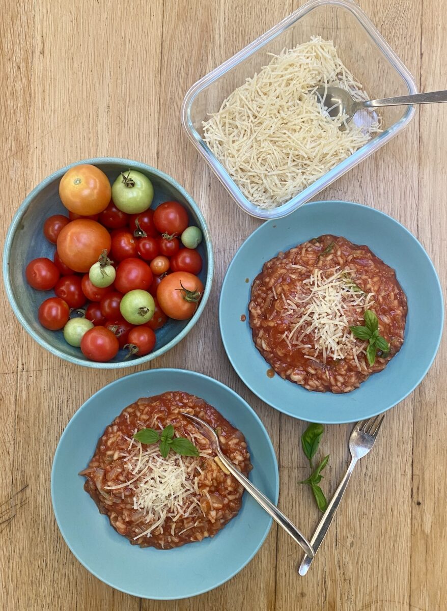 2 bowls of tomato risotto in duck egg blue bowls, with a dish of fresh tomatoes and parmesan. 