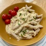 easy green tomato sauce with pasta in a mustard coloured bowl on a blue striped plate.