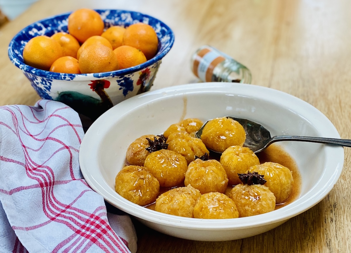 Christmas clementines in a cream coloured bowl with a silver spoon. A blue patterned bowl full of more clementines is nearby, and a red striped tea-towel. 