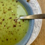 frozen pea soup in a blue bowl, on a white plate, with a spoon in the soup.