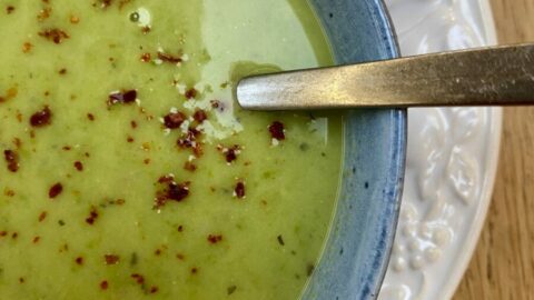 frozen pea soup in a blue bowl, on a white plate, with a spoon in the soup.