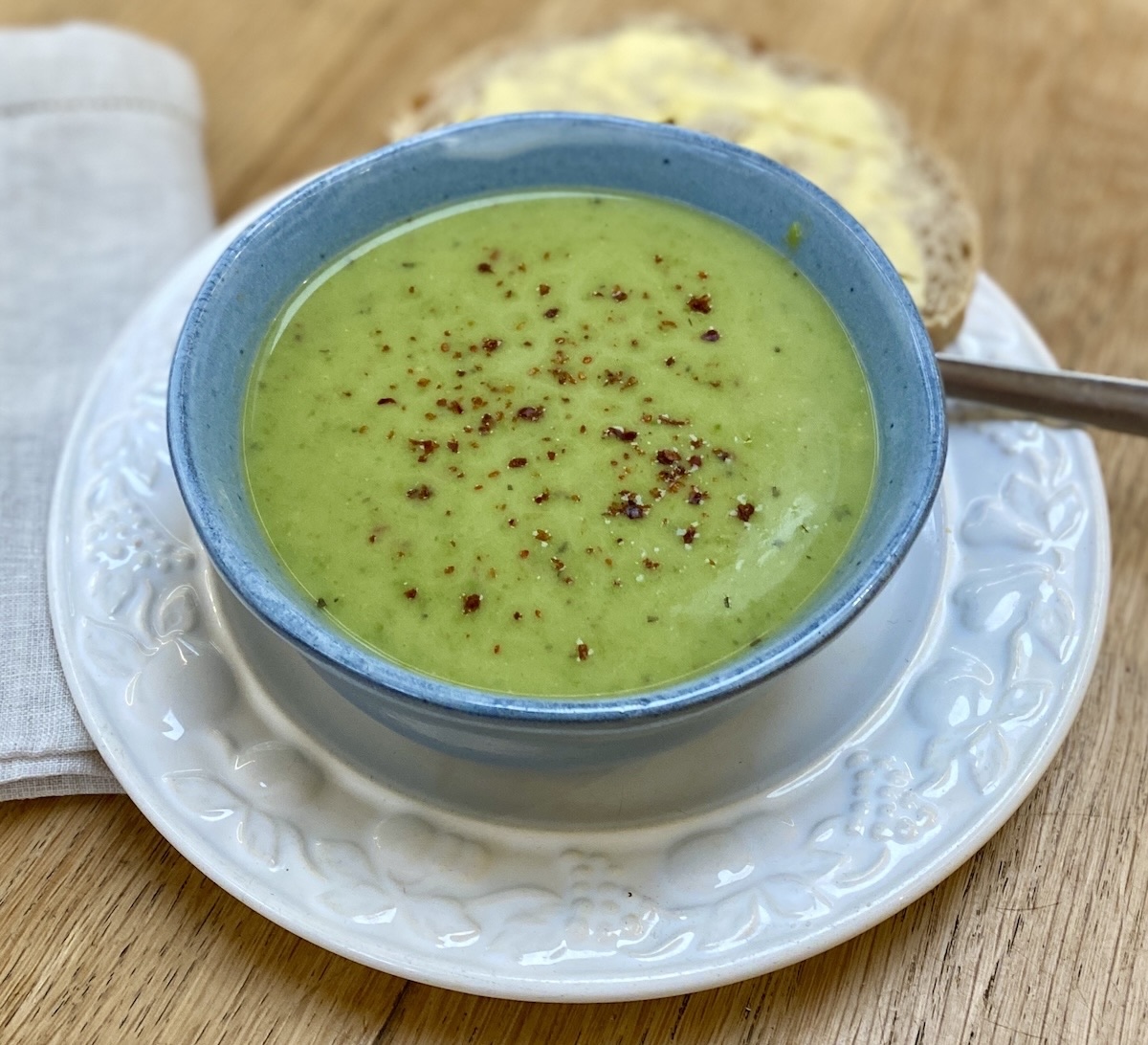 green pea soup in a blue bowl, on a white plate. 