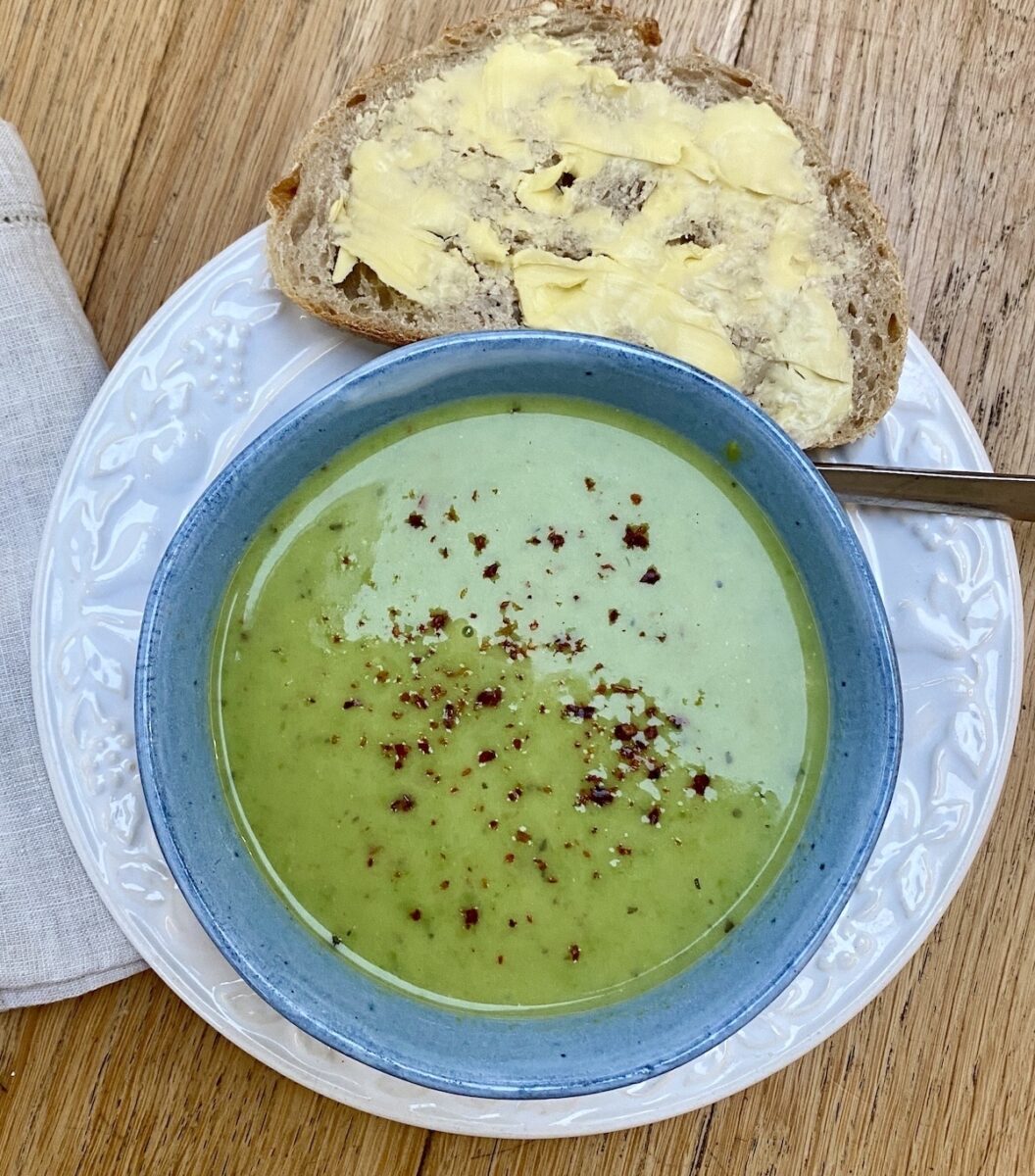 green pea soup in a blue bowl on a white plate, with a slice of bread and butter on the side. 