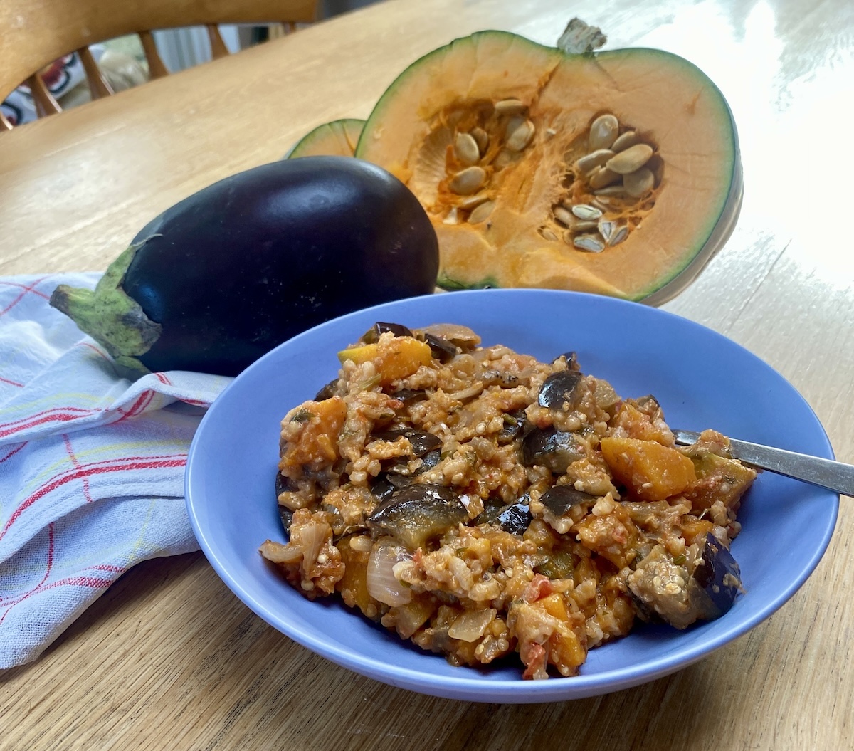 vegetarian pumpkin risotto in a shallow blue bowl with an aubergine and pumpkin half nearby