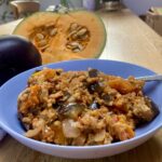 vegetarian risotto in a shallow blue bowl with a whole aubergine and half a pumpkin nearby.