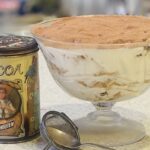 Tiramisu Panetonne in a large glass bowl, with a tin of cocoa and a small sieve.