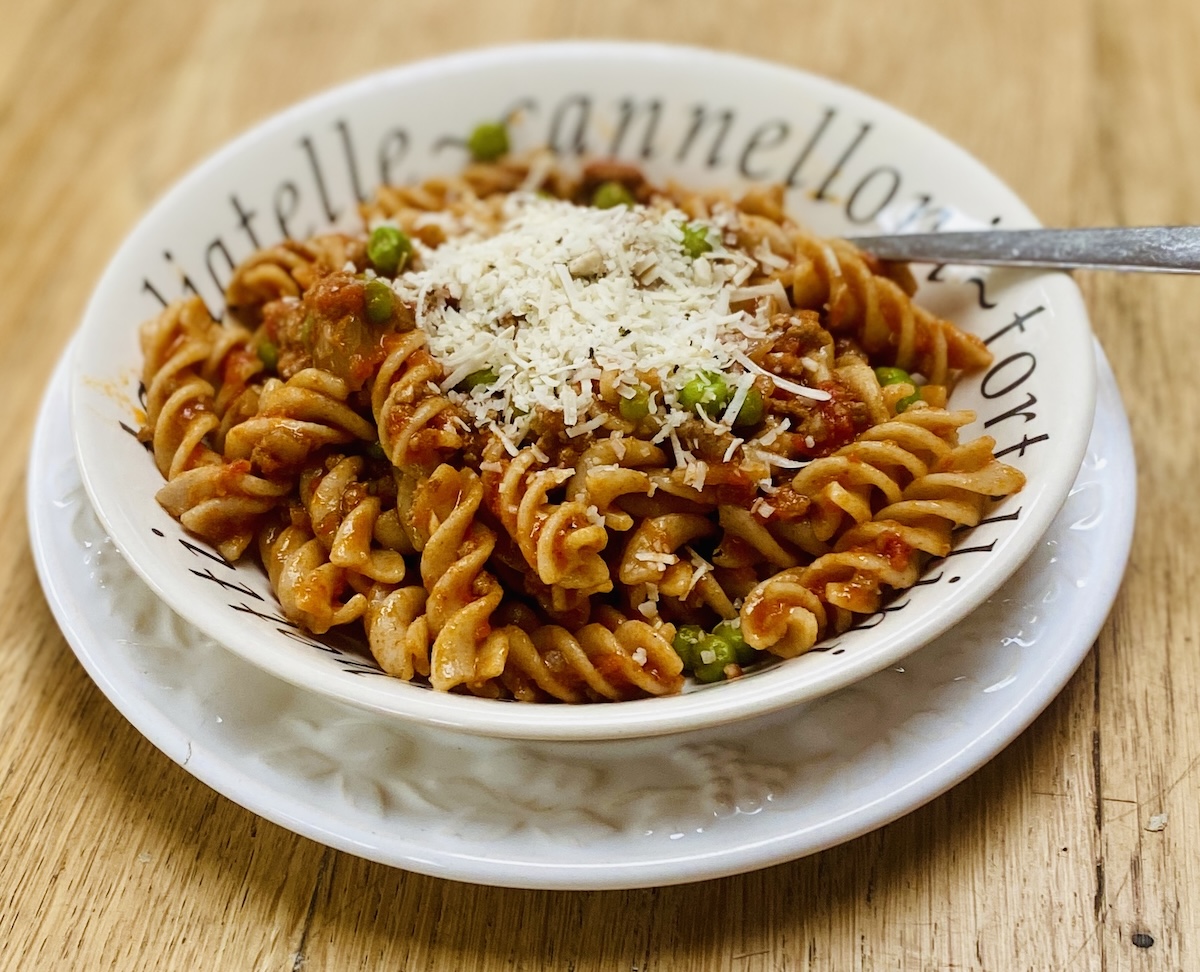 A white dish filled with lamb ragu and wholemeal farfalle, on a white plate.