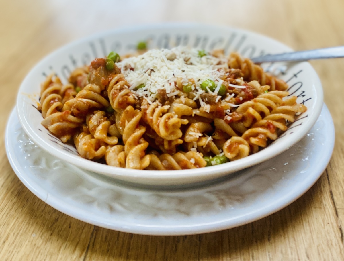 A white dish filled with lamb ragu and wholemeal farfalle, on a white plate.