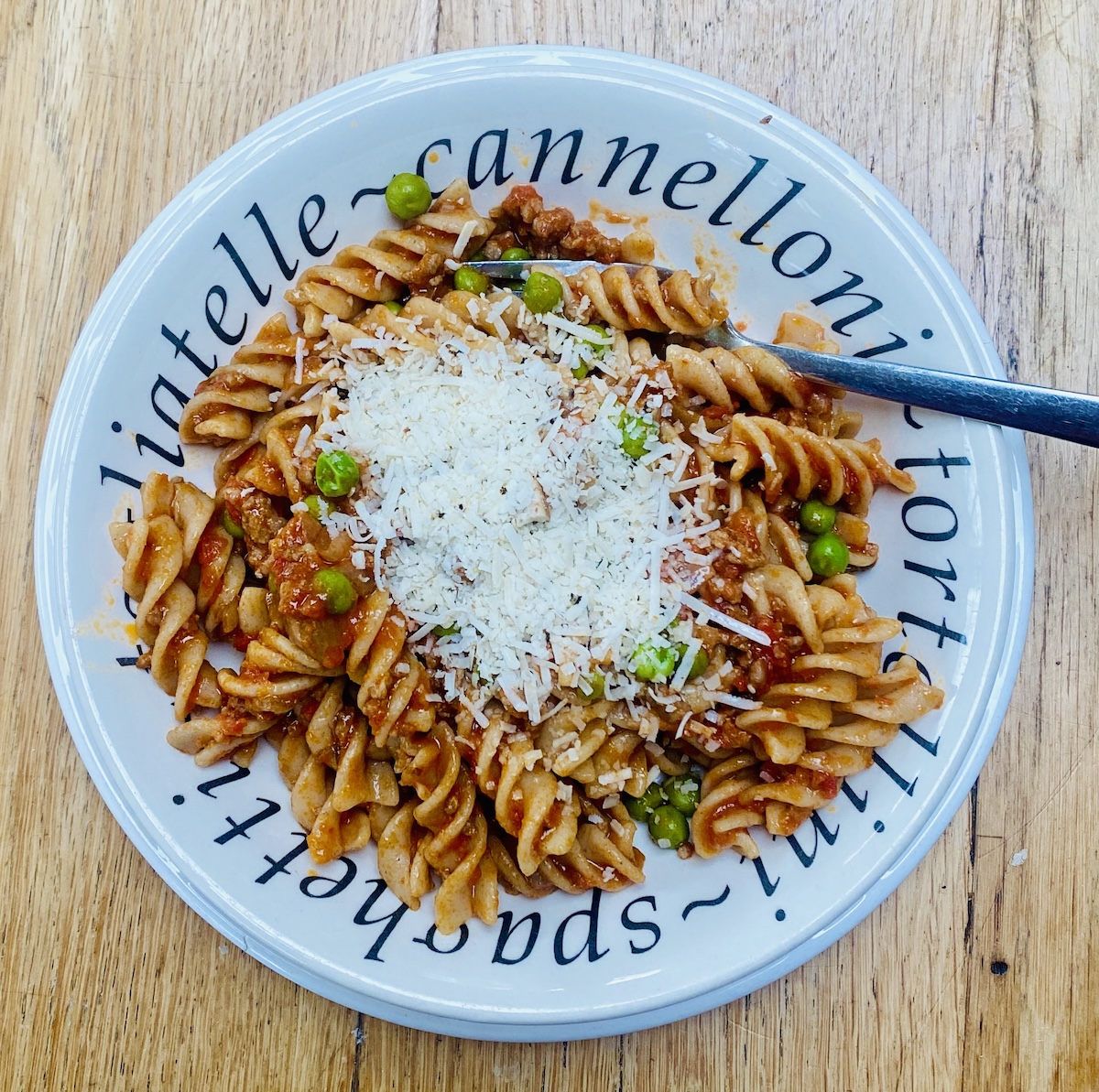 A white dish filled with lamb ragu and wholemeal farfalle, on a white plate.