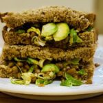 Spiced lentils in a granary sandwich, two halves stacked on a white plate.