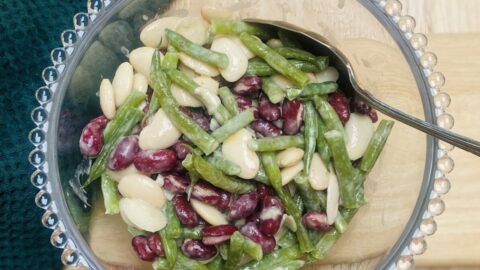3 bean salad in a glass bowl with glass bobbles all round the rim, with a spoon.