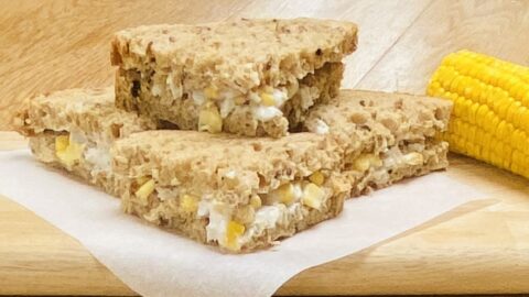 a chicken and sweetcorn sandwich, cut into quarters, on greaseproof paper and a wooden board.