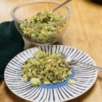 crunchy broccoli salad in a glass bowl, with a spoon. A portion on a blue striped plate.