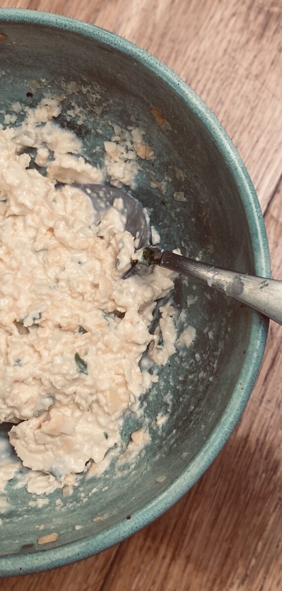a close up view of a cheese and onion sandwich filling, in a duck egg blue bowl, with a spoon. 